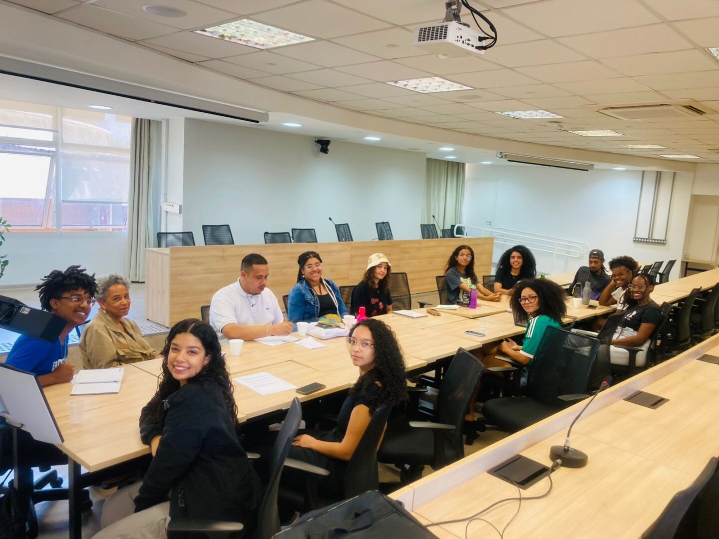 13 pessoas reunidas em um auditório. Todos estão sentados e olham em direção à foto. 