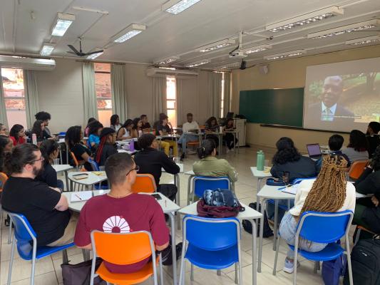 Os alunos agora estão dentro de uma sala de aula, com as janelas entreabertas, sentados nas carteiras em semicírculo, em direção a lousa e ao projetor da sala de aula, assistindo um vídeo do curso Ubunto.