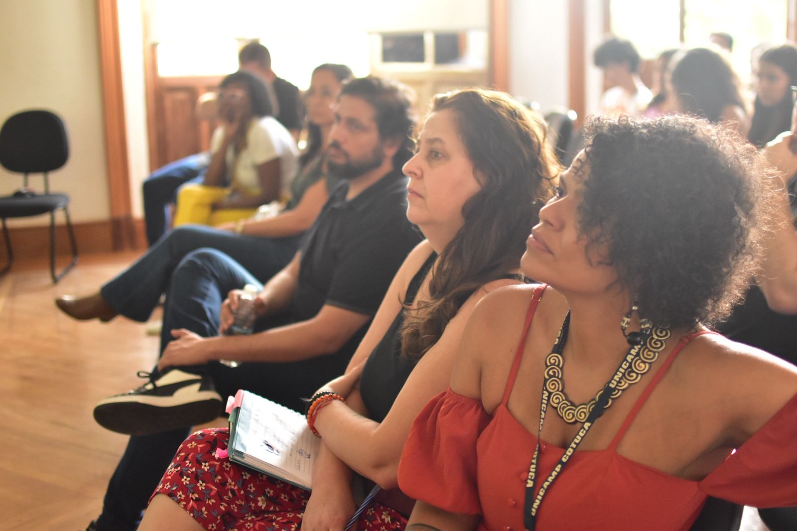Prof. Débora à frente escutando as falas, sentada com outras pessoas durante a Unicamp Afro